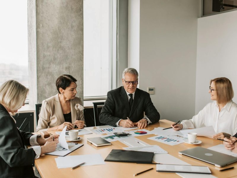 A group of professionals discussing business documents during a meeting in a modern office setting.